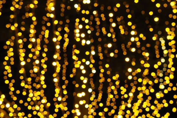 Bokeh röfleleri. Karanlıkta sarı ve altın rengi yanıp sönüyor. Şenlik arka planı. Bulanık defocus. Şehir sokaklarının dekorasyonu. Bir sürü sarı top. Birçok sarı, beyaz ve turuncu daireler