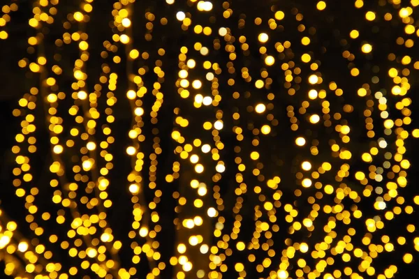 Bokeh röfleleri. Karanlıkta sarı ve altın rengi yanıp sönüyor. Şenlik arka planı. Bulanık defocus. Şehir sokaklarının dekorasyonu. Bir sürü sarı top. Birçok sarı, beyaz ve turuncu daireler