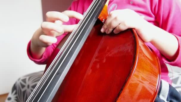大提琴上的Picicato一个穿着粉色夹克的小女孩用手指弹奏着无弓大提琴的披萨 音乐学校的初级小提琴学习 — 图库视频影像
