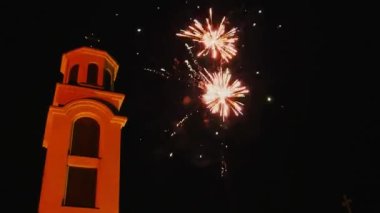 Fireworks for Christmas. Beautiful flashes and flashes of fire and fireworks against the background of the night sky and a Christian church with a cross. Multiple explosions of pyrotechnics