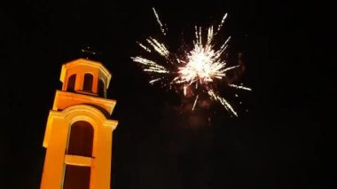 Fireworks for Christmas. Beautiful flashes and flashes of fire and fireworks against the background of the night sky and a Christian church with a cross. Multiple explosions of pyrotechnics
