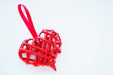 Red braided heart with a silk ribbon on a white background. Valentine's Day. copyspace. A nice souvenir - a pendant at an angle