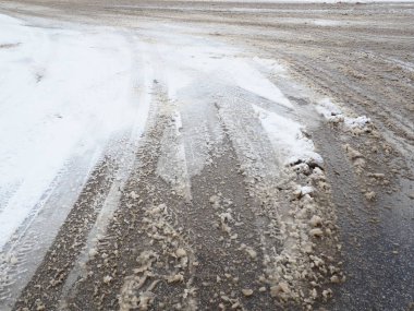 Yol kenarında kar yağışı var. Zorlu sürüş koşulları. Islak, kaygan, ayak izleri olan bir kaldırım. Tehlikeli bir buz. Kışın çamurlu hava. Araba lastiği izleri. Temizlik için belediye hizmetleri.