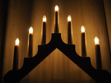 Schwibbogen kemeri, üçgen bir şamdan şeklinde. Sarı arka plan. Akşam, romantik, şenlikli, dini ya da mistik atmosfer. Mum ışığına benzeyen yanan ampuller.