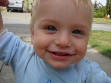 Oğlanın sarı saçları var ve mavi bir bluz giyiyor. İlk yaprak döken dişler açık ağızdan görülebilir..