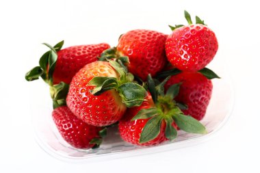 Beyaz arka planda plastik bir pakette olgun çilekler. Konteynırda müşterilere satılacak taze meyveler. Yemeği taze tutmak. Sağlıklı gıda, vitaminler ve mikro elementler