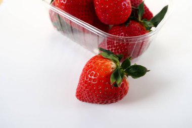 Beyaz arka planda plastik bir pakette olgun çilekler. Konteynırda müşterilere satılacak taze meyveler. Yemeği taze tutmak. Sağlıklı yiyecekler. Konteynırdan bir çilek çıkarıldı.