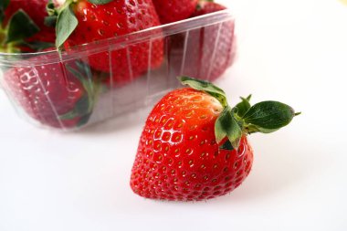 Beyaz arka planda plastik bir pakette olgun çilekler. Konteynırda müşterilere satılacak taze meyveler. Yemeği taze tutmak. Sağlıklı yiyecekler. Konteynırdan bir çilek çıkarıldı.