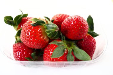 Beyaz arka planda plastik bir pakette olgun çilekler. Konteynırda müşterilere satılacak taze meyveler. Yemeği taze tutmak. Sağlıklı gıda, vitaminler ve mikro elementler
