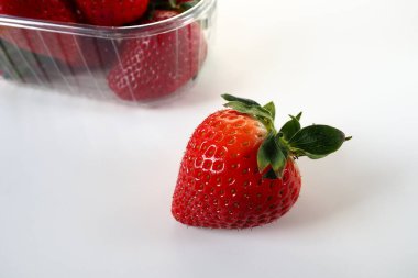 Beyaz arka planda plastik bir pakette olgun çilekler. Konteynırda müşterilere satılacak taze meyveler. Yemeği taze tutmak. Sağlıklı yiyecekler. Konteynırdan bir çilek çıkarıldı.