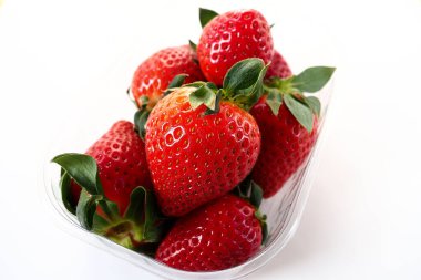 Beyaz arka planda plastik bir pakette olgun çilekler. Konteynırda müşterilere satılacak taze meyveler. Yemeği taze tutmak. Sağlıklı gıda, vitaminler ve mikro elementler