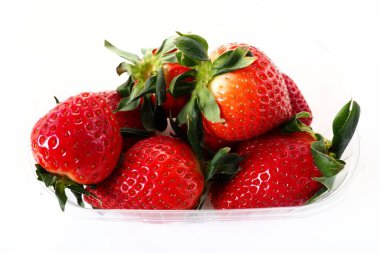 Beyaz arka planda plastik bir pakette olgun çilekler. Konteynırda müşterilere satılacak taze meyveler. Yemeği taze tutmak. Sağlıklı gıda, vitaminler ve mikro elementler