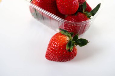 Beyaz arka planda plastik bir pakette olgun çilekler. Konteynırda müşterilere satılacak taze meyveler. Yemeği taze tutmak. Sağlıklı yiyecekler. Konteynırdan bir çilek çıkarıldı.
