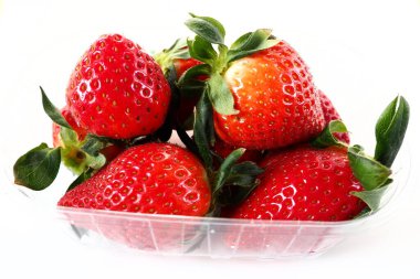 Beyaz arka planda plastik bir pakette olgun çilekler. Konteynırda müşterilere satılacak taze meyveler. Yemeği taze tutmak. Sağlıklı gıda, vitaminler ve mikro elementler