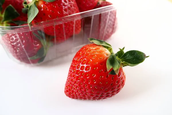 Beyaz arka planda plastik bir pakette olgun çilekler. Konteynırda müşterilere satılacak taze meyveler. Yemeği taze tutmak. Sağlıklı yiyecekler. Konteynırdan bir çilek çıkarıldı.