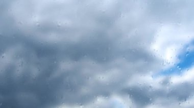 Mavi gökyüzüne karşı hızlı hareket eden bulutlar. Bulutlu kümülüs bulutları rüzgarda gittikçe daha alçaktan ve daha hızlı hareket eder. Meteoroloji ve hava tahmini. Bardaktan aşağı yağmur damlaları akıyor. Fırtına rüzgarı zaman ayarlı. Sulu cam.