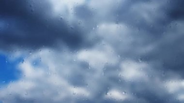 Mavi gökyüzüne karşı hızlı hareket eden bulutlar. Bulutlu kümülüs bulutları rüzgarda gittikçe daha alçaktan ve daha hızlı hareket eder. Meteoroloji ve hava tahmini. Bardaktan aşağı yağmur damlaları akıyor. Fırtına rüzgarı zaman ayarlı. Yumuşak odak