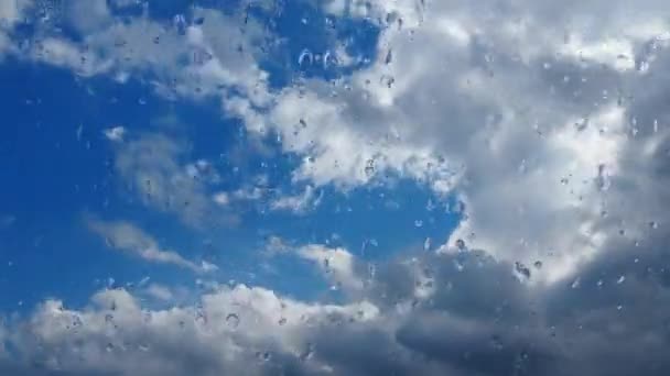 Fast-moving clouds against a blue sky. Cloudiness cumulus clouds move lower and faster in the wind. Meteorology and weather forecast. Raindrops run down the glass. Storm wind timelapse. Misted glass. — ストック動画