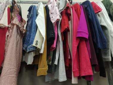 Elbiseler askılarda asılı. İkinci el mağazasının çeşitli ürünleri. Çocuk gömlekleri, bluzlar, askıda asılı süveterler, müşterilere satılmaya hazır. Para biriktiriyorum. Belgrad Sırbistan 22 Nisan 2022 