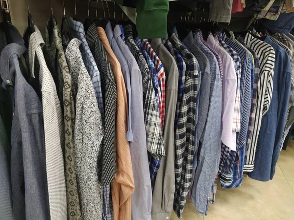 Elbiseler askılarda asılı. İkinci el mağazasının çeşitli ürünleri. Erkeklerin gömlekleri askıda asılı, müşterilere satılmaya hazır. Krizde para biriktiriyorum. Ucuz alışveriş. Damalı, çizgili, sade erkek gömlekleri..