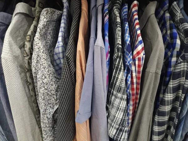 Clothes hung on hangers. Assortment of second hand store. Mens shirts hanging on a rack, ready for sale to customers. Saving money in crisis. Cheap shopping. Checkered, striped, plain mens shirts