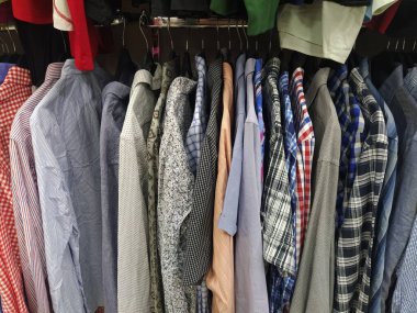 Elbiseler askılarda asılı. İkinci el mağazasının çeşitli ürünleri. Erkeklerin gömlekleri askıda asılı, müşterilere satılmaya hazır. Krizde para biriktiriyorum. Ucuz alışveriş. Damalı, çizgili, sade erkek gömlekleri..