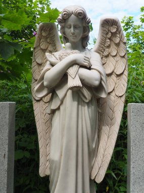 An angel with a dove. Sculpture in the cemetery. The figure of an angel with wings holding a bird in his arms. Lamentation for the deceased. Headstone monument on a Christian grave. Sadness sorrow