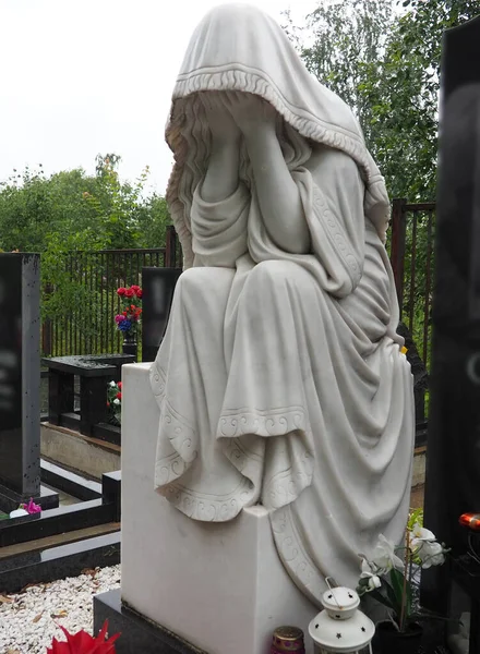 Weeping woman. Sculpture in the cemetery. The figure of a mother, wife or woman in a hood or stole. Lamentation for the deceased. Tombstone on a Christian grave. Sadness and grief.