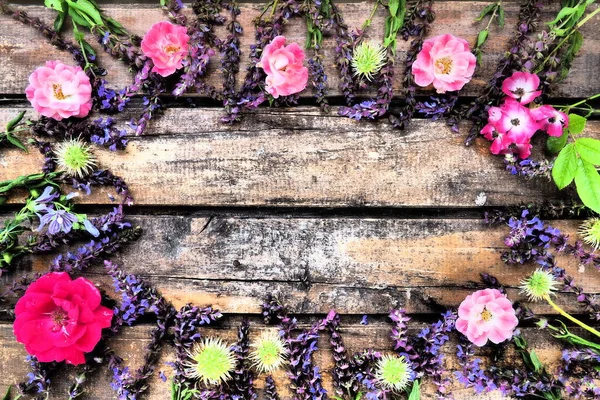 Flowers in a circle on a wooden background. Postcard for the holiday. Roses, geraniums, lavender, sage and hairy chestnuts are placed along the edges on dark boards. Background copy space, flat lay