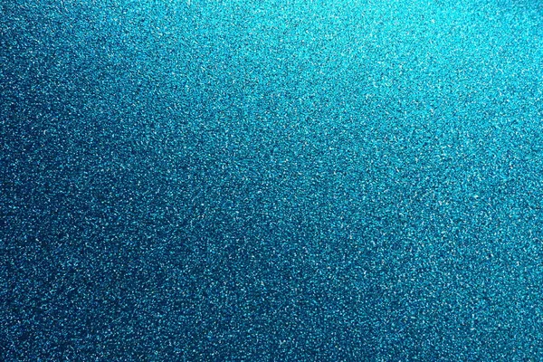 Deep blue. Texture of rough paper or cardboard. Defocused bokeh sparkles and shining. Festive blue background with illuminated gradient from top right. Deep blue sapphire