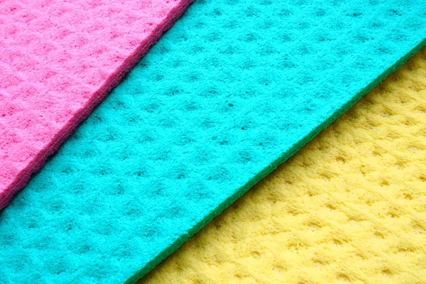 A set of cleaning wipes, microfiber cloths or sponges for the kitchen, three multi-colored cloths. Sponge fibers sponge texture pattern surface close-up background. Pink, blue and yellow