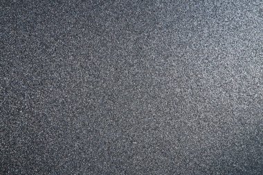 Black or dark gray background with shine. Texture of rough paper or cardboard. Defocused bokeh sparkles and shining from above. Festive black background with illuminated gradient.