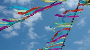 Colored ribbons flutter in the wind. A blue sky with clouds. Festive decoration of streets, decorations for religious rituals. Garlands with light bulbs are hung. Red, green, blue, purple, yellow.