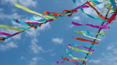 Colored ribbons flutter in the wind. A blue sky with clouds. Festive decoration of streets, decorations for religious rituals. Garlands with light bulbs are hung. Red, green, blue, purple, yellow.