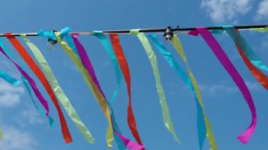 Colored ribbons flutter in the wind. A blue sky with clouds. Festive decoration of streets, decorations for religious rituals. Garlands with light bulbs are hung. Red, green, blue, purple, yellow.