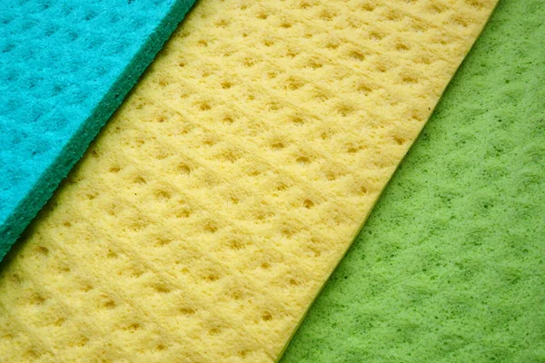 A set of cleaning wipes, microfiber cloths or sponges for the kitchen, three multi-colored cloths. Sponge fibers sponge texture pattern surface close-up background. Green, blue and yellow.