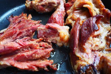 Roasted smoked pork shoulder or knee. Delicious meat on a black baking sheet with drops of vegetable oil, taken out of the oven. Pork delicacy for dinner in a restaurant and family lunch. Red meat.