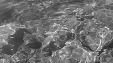 Şeffaf deniz tuzlu su dokusu. Su yüzeyinin üst görüntüsü ve dalgalanmalar. Su dalgaları arka planda. Alglerle kayalık taban kristal su yoluyla görülebilir. Tek renkli ağır çekim