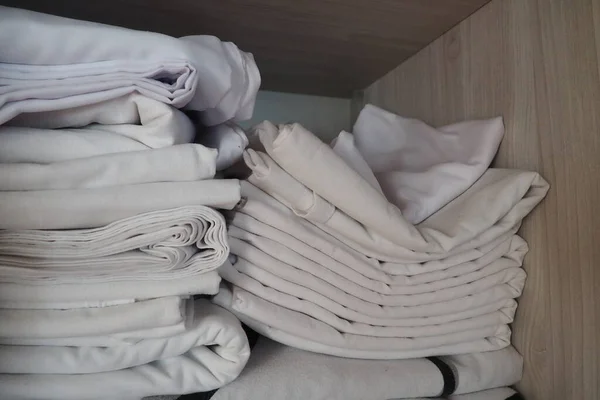 The white linens are stacked in the closet. Internal contents of a linen closet. Household organization. Hygienic conditions for sleep. Fabrics and bed sheets in half open white closet or wardrobe.