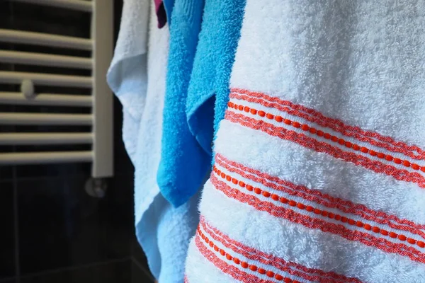 Towels hang next to a heated towel rail, wall radiator or radiator. White, blue, pink, red towels. Organization of household items in the bathroom. Housekeeping