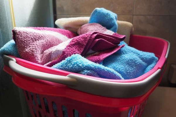 Towels in the laundry basket. Blue and pink cotton terry towels are thrown into a pink plastic basket. Housekeeping. Storing and separating laundry before washing. Light from above from an open window