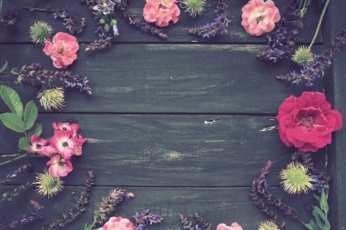 Ahşap bir arka planda daire şeklinde çiçekler. Tatil için kartpostal. Güller, sardunyalar, lavantalar, adaçayı ve kıllı kestaneler koyu tahtaların kenarlarına yerleştirilir. Arkaplan kopyalama alanı, düz uzanma