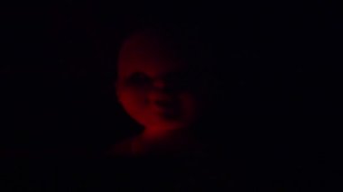 Karanlıktaki kırmızı ve mavi ışıklı korkunç bebek. Cadılar Bayramı teması, korku ve kabuslar. Uğursuz, cansız, şeytani bir yüz ve siyah saç.