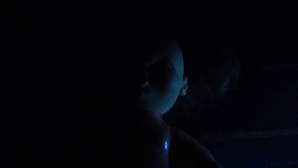 可怕的娃娃在黑暗中与红色和蓝色的灯 万圣节的主题 恐怖和噩梦 一个不祥的 无生命的魔鬼脸和黑发 — 图库视频影像