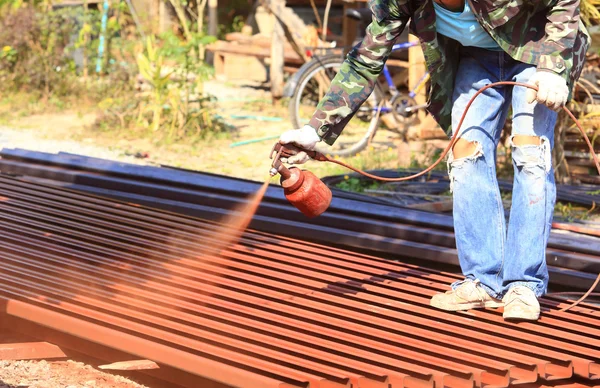 Pracownik spray czerwony kolor na dachu ze stali do budowy domu — Zdjęcie stockowe