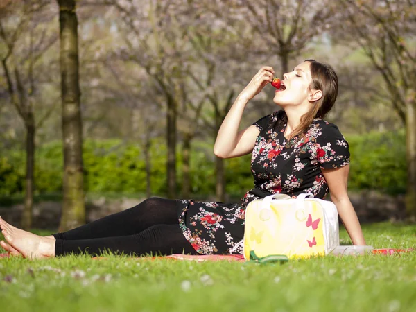 Mooi meisje eten van een aardbei tijdens een picknick in het voorjaar — Stockfoto