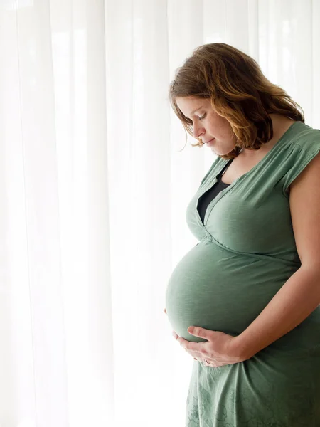 Pregnant young woman looking at her belly — Stock Photo, Image