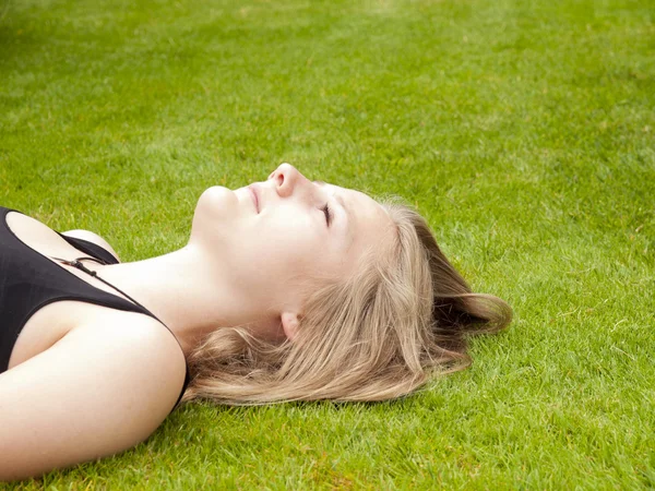 Mooie tienermeisje liggend op haar rug in het groene gras — Stockfoto