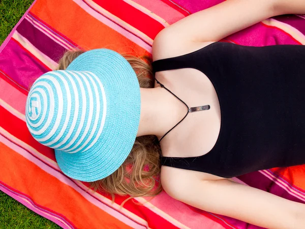 Tiener meisje met een hoed die betrekking hebben op haar gezicht liggend op haar rug op een kleurrijk tapijt — Stockfoto