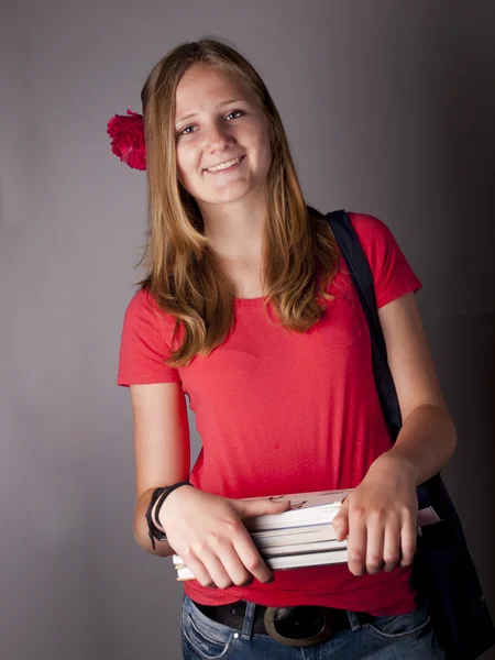 Jonge vrouwelijke tiener student boeken over een grijze achtergrond te dragen — Stockfoto